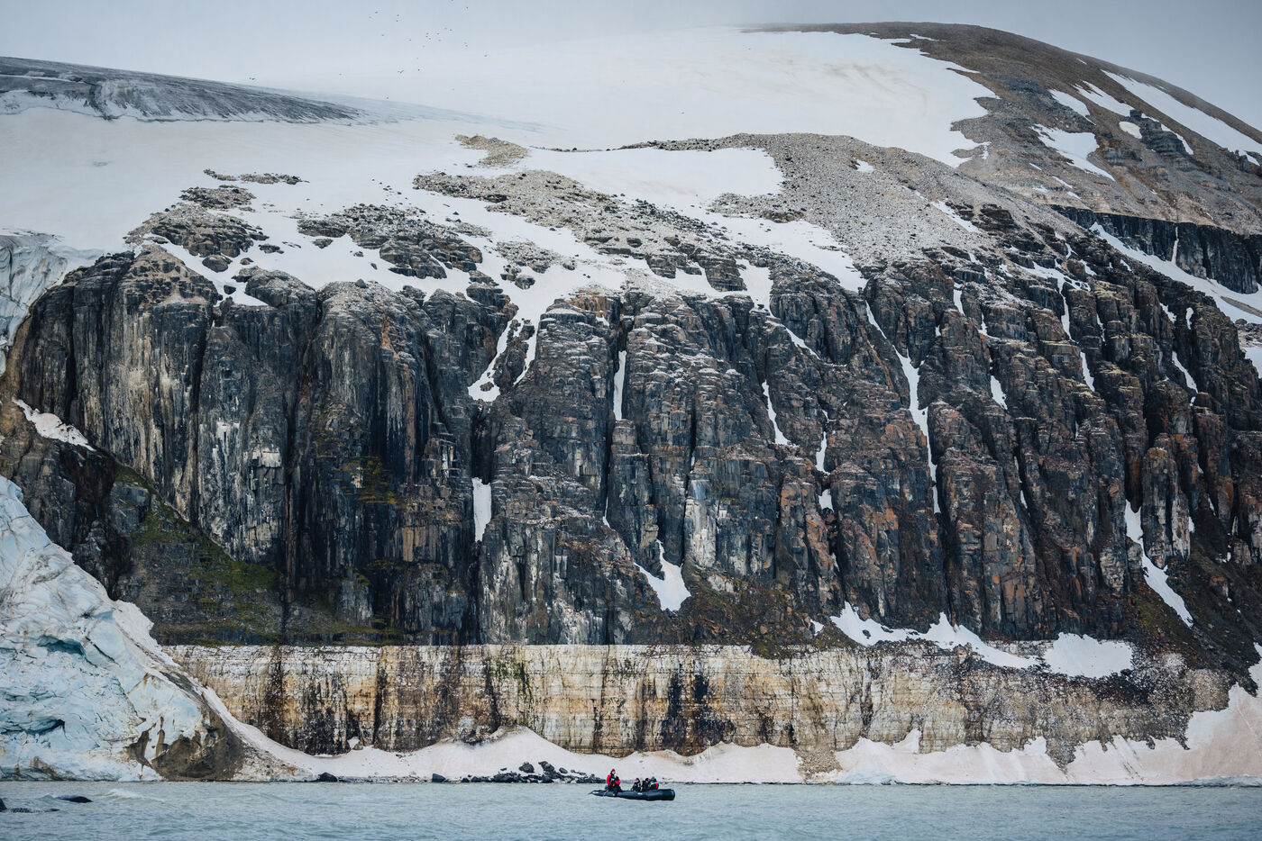 Zodiacs at the foot of a snow-capped cliff band