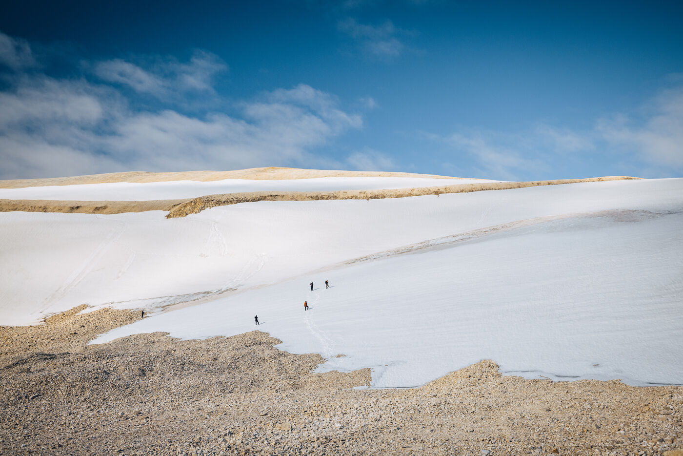 Tiny figures walking across a snowfield below a blue sky