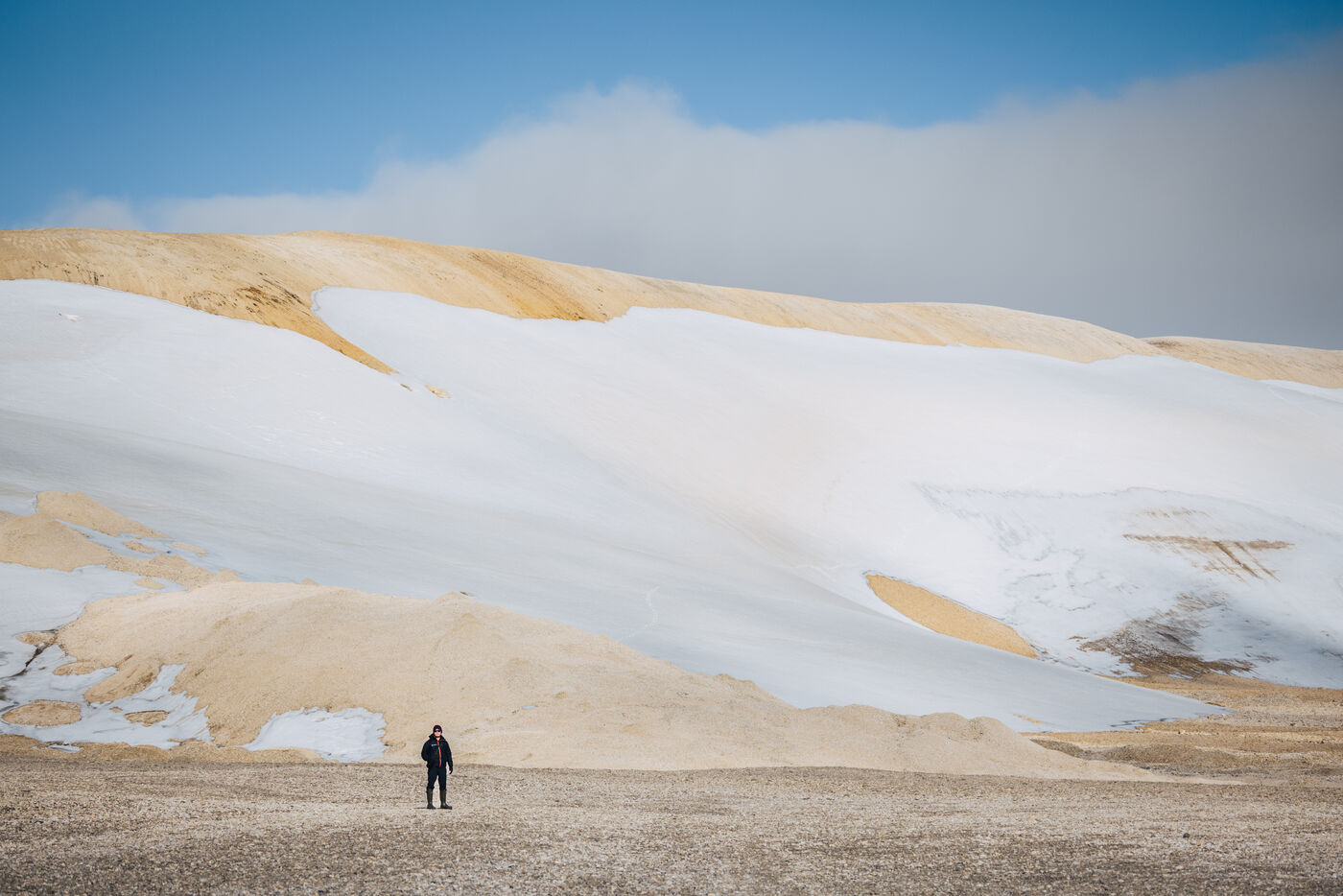 Lone figure on gravel below snow-covered hills