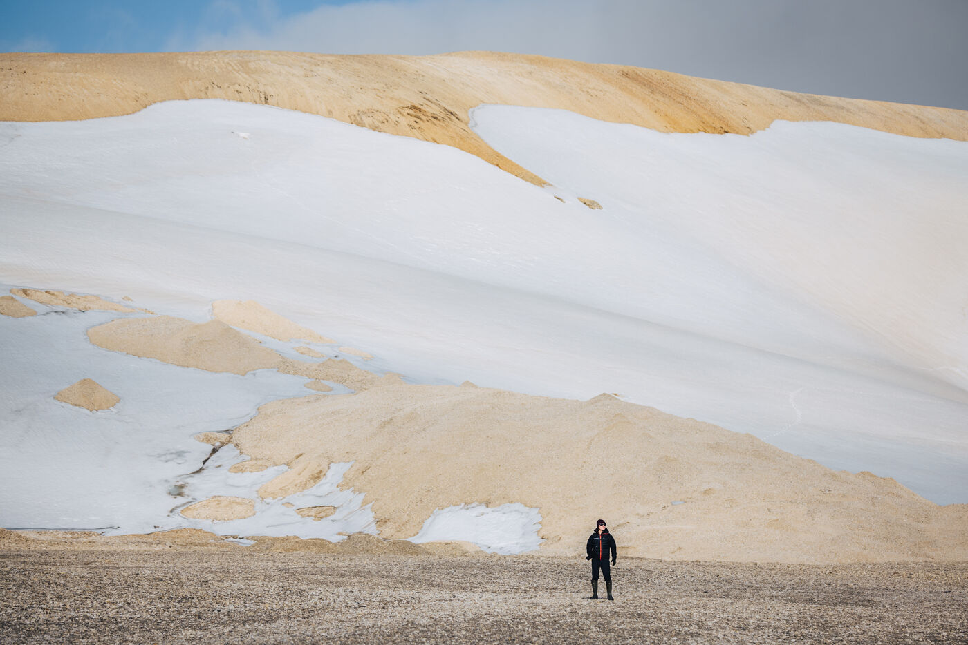 Lone figure on gravel flats below snow-covered slopes
