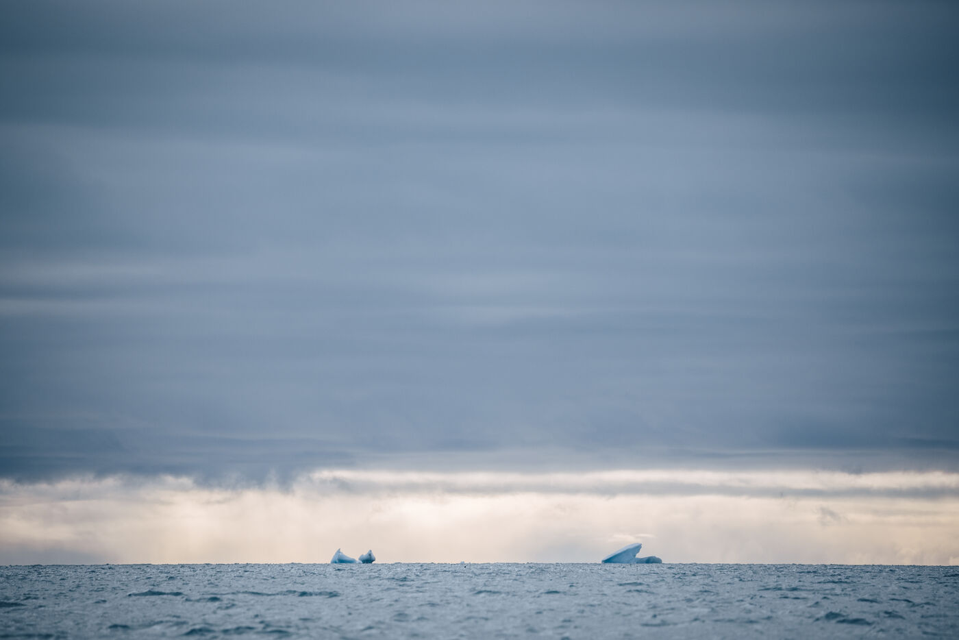 Two small icebergs visible on flat gray horizon
