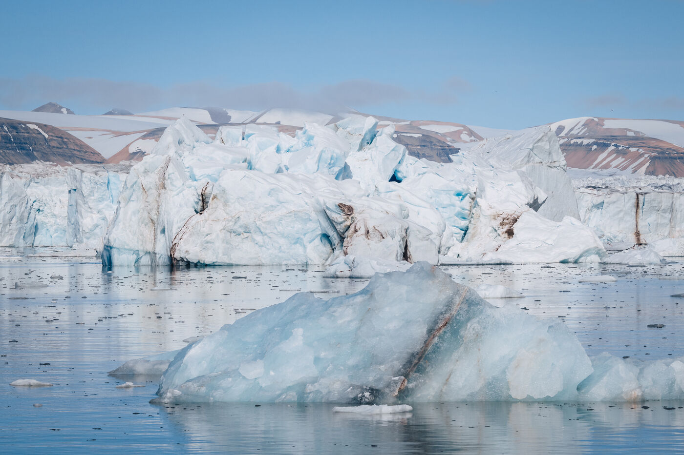 Massive glacier terminus meeting calm water, turquoise ice visible