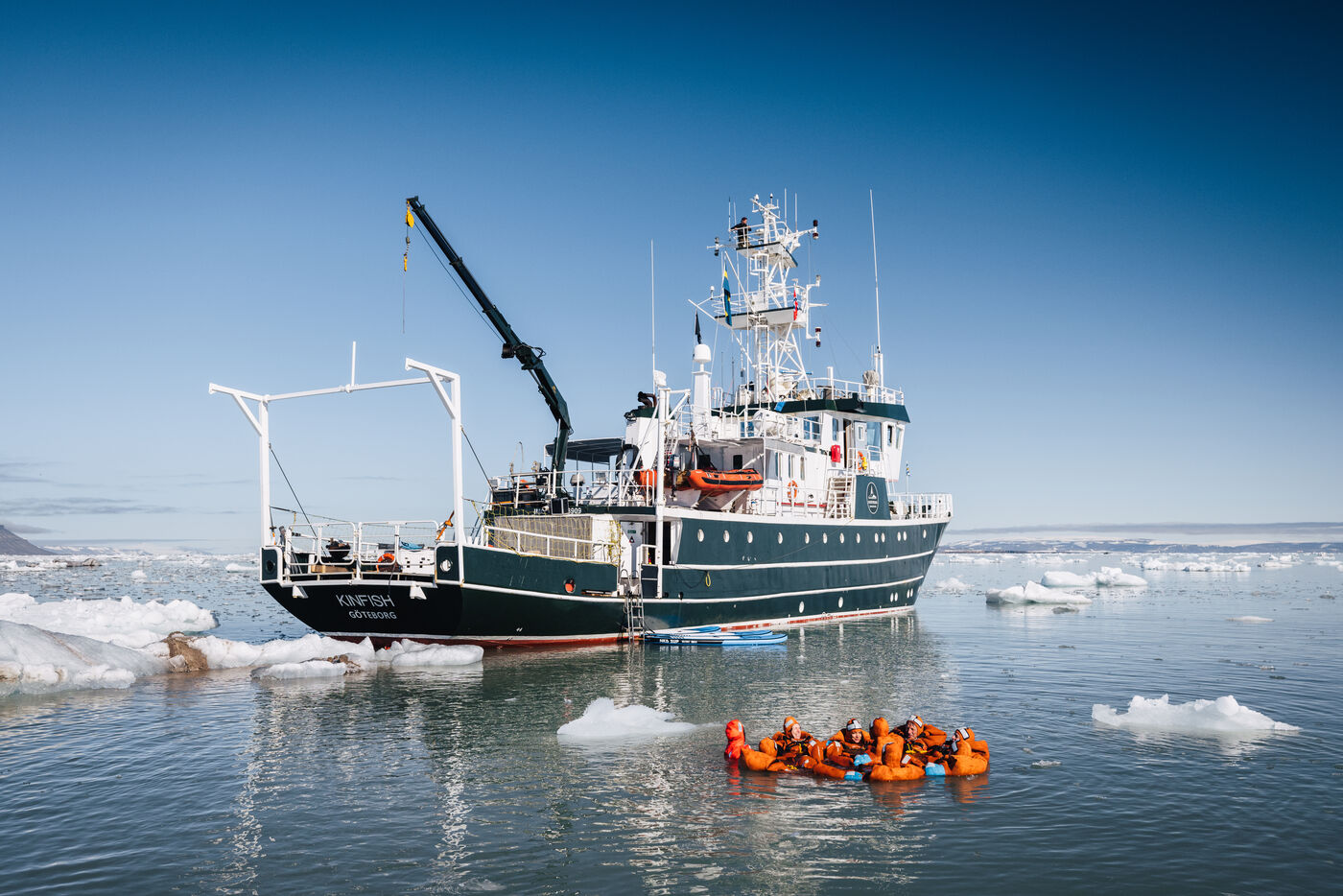 Multiple divers in orange suits in water surrounding ship