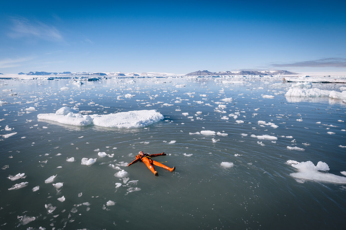 Wide view of fjord with iceberg and swimmers