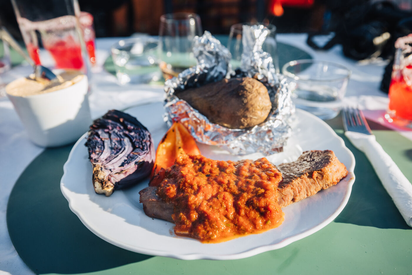 Plate of barbecue with red sauce, a foil-wrapped baked potato and charred red cabbage