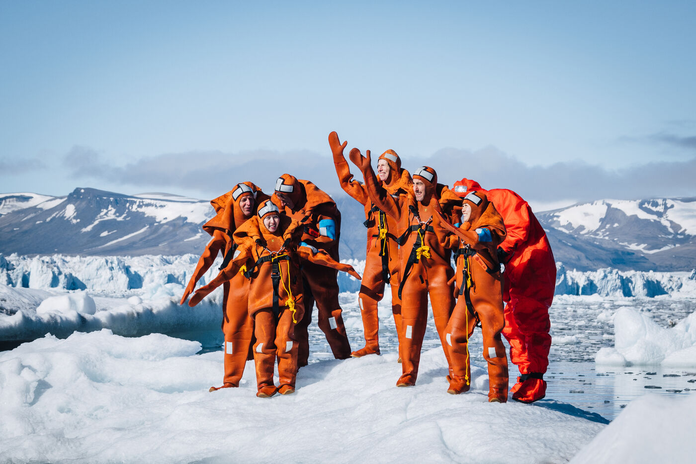 Group of people in orange suits on ice with fjord behind