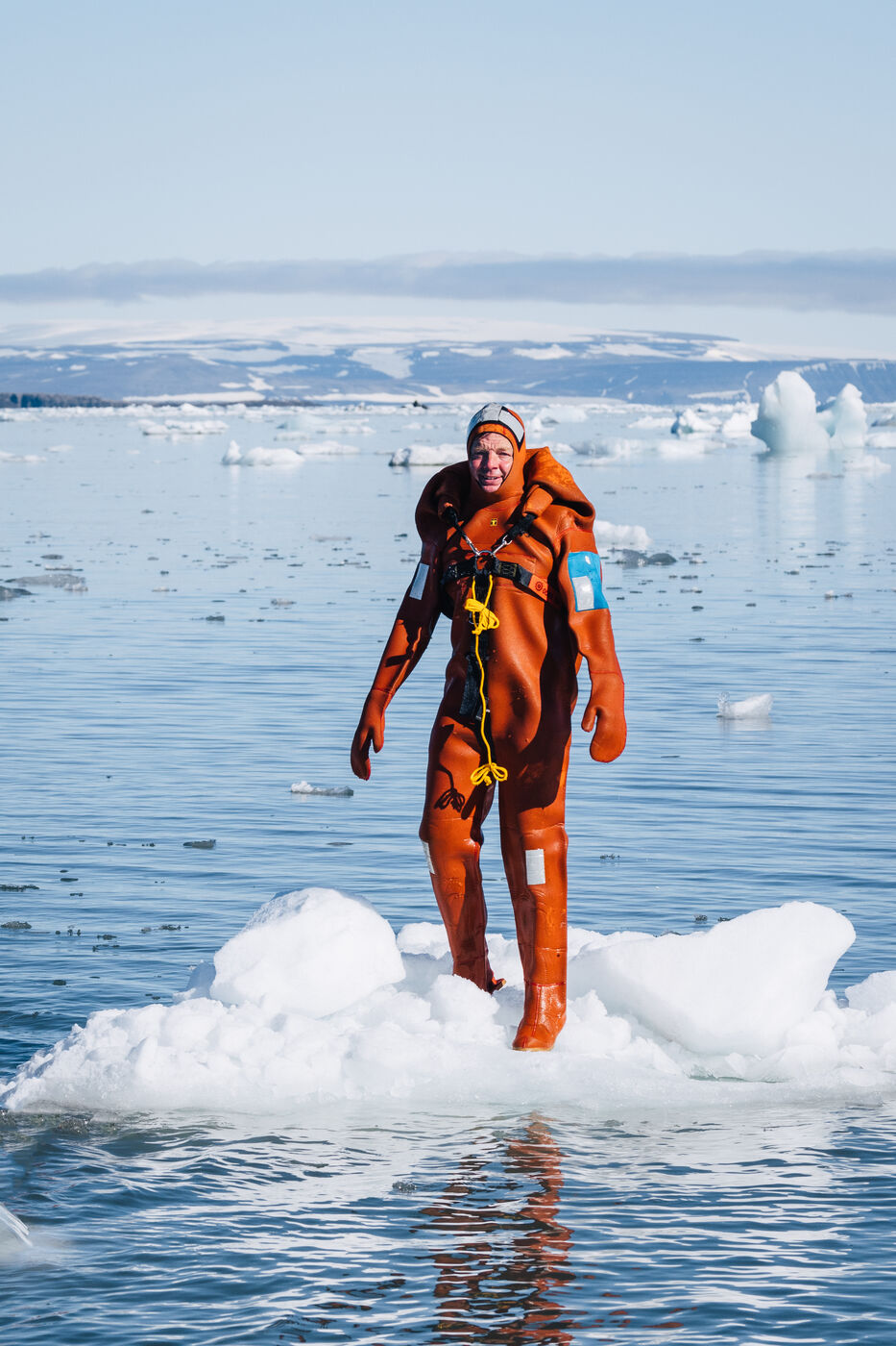 Person in an orange survival suit standing on a small ice floe