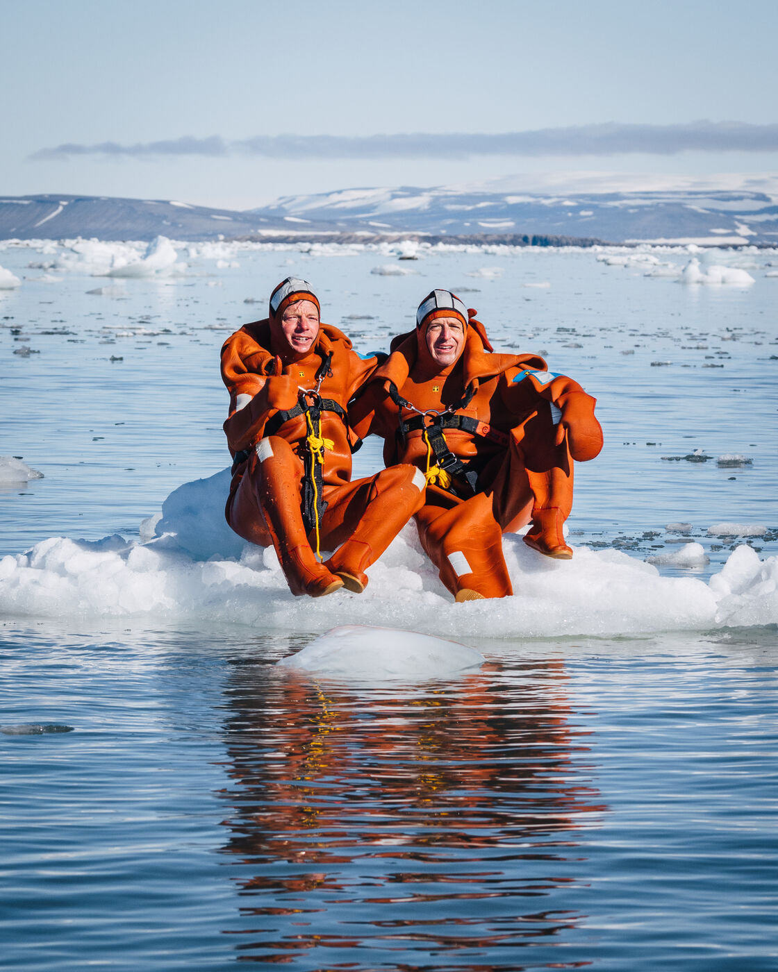 Two people in orange survival suits sitting on an ice floe