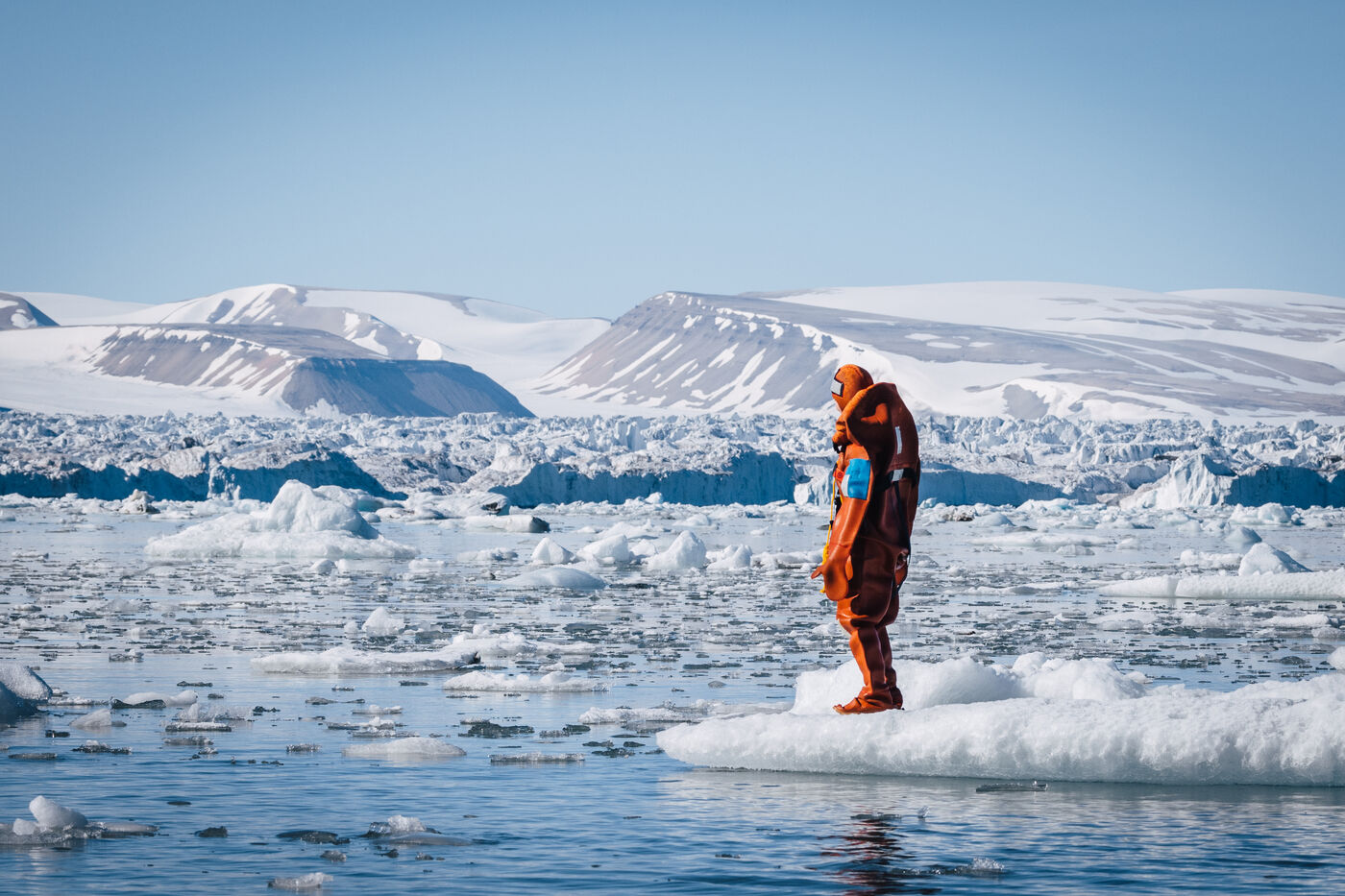 Diver standing on ice facing away toward fjord mountains