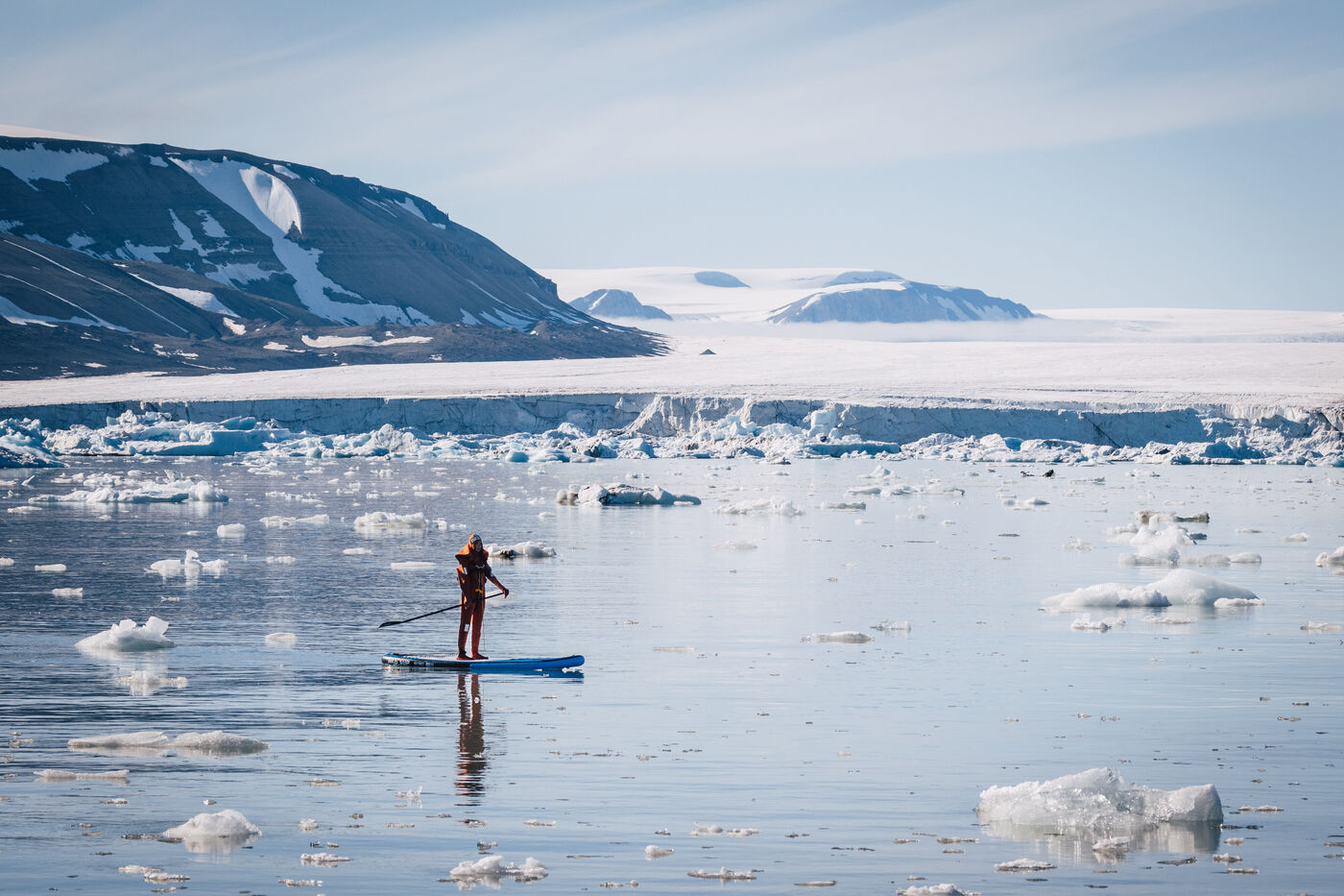 Paddleboarder gliding across still water among ice floes