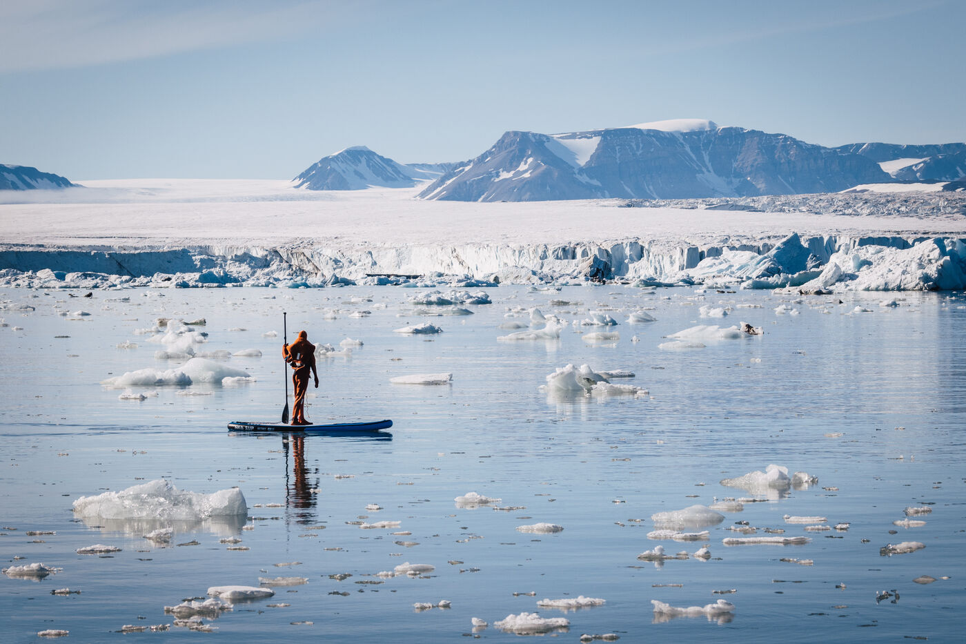 Person on paddleboard in water with mountains and ice