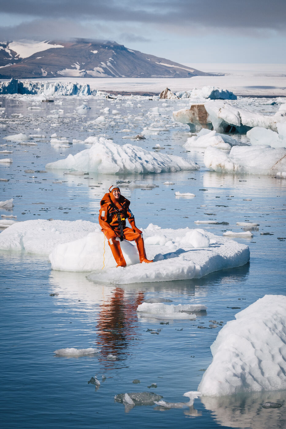 Person in an orange survival suit sitting on an ice floe