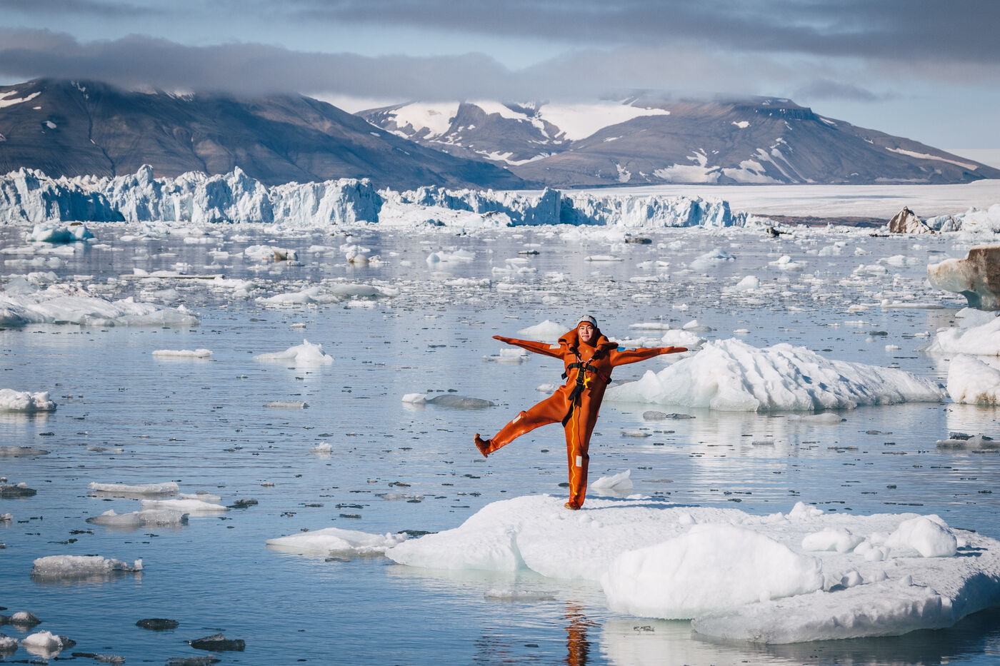 Person in an orange survival suit balancing on one leg atop an ice floe