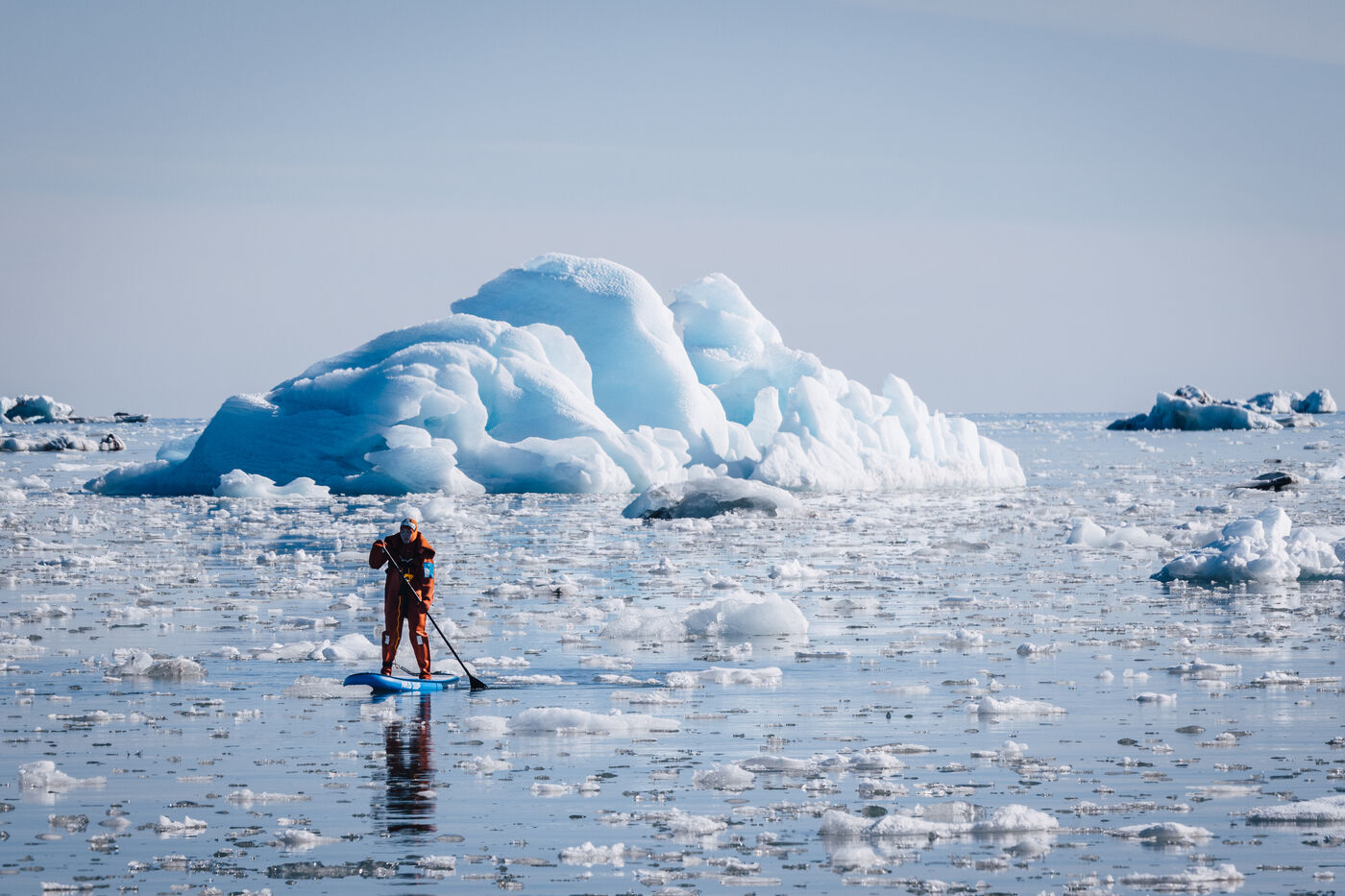 Paddleboarder passing a large blue iceberg