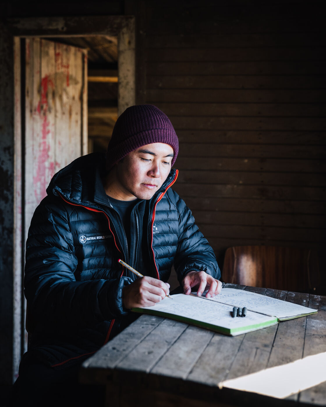 Person writing in notebook inside rustic wooden cabin