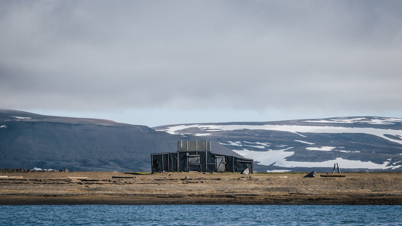 Trapper's cabin on the flat shore below snow-patched hills