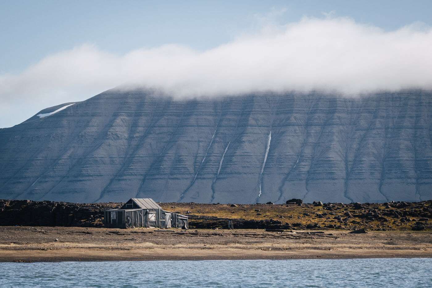 Trapper's cabin dwarfed by a cloud-capped, snow-streaked mountain