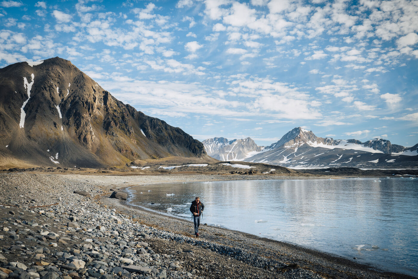 Lone figure walking across barren tundra with dramatic mountainous fjord landscape