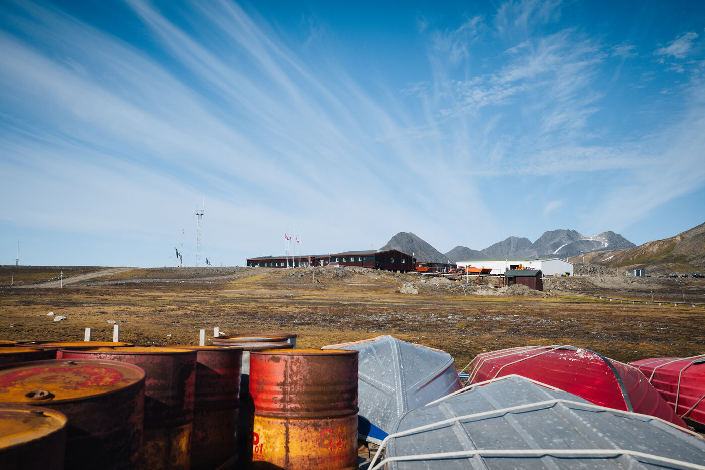 Colorful barrels and equipment scattered on tundra near research structures and mountains