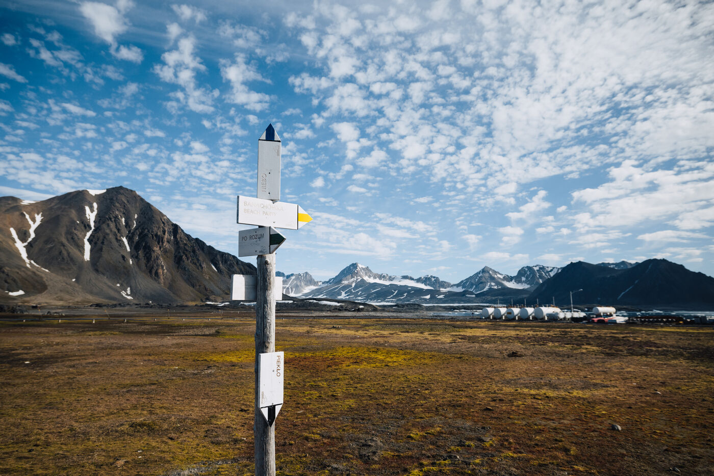 Signpost on the tundra in front of the Polish station, mountains and glacier beyond