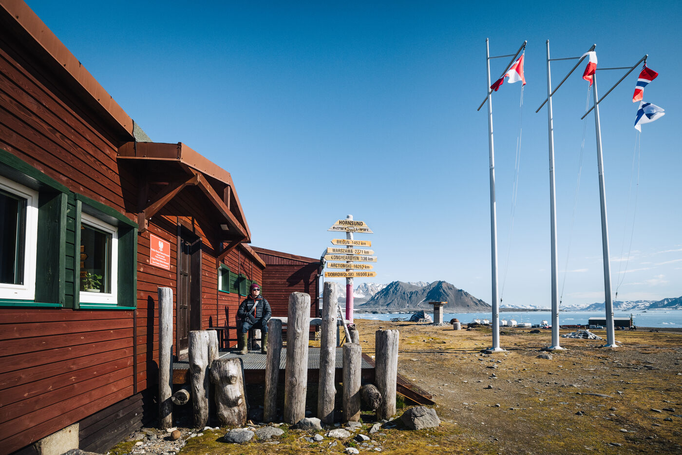 Red wooden station buildings with flagpoles and a signpost under a blue sky