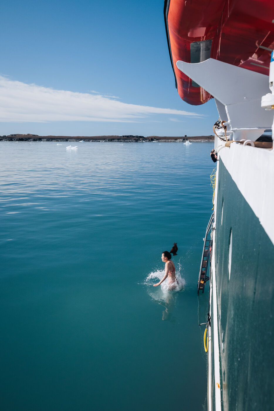 Person in icy Arctic fjord water, committed to the cold, ship visible in background