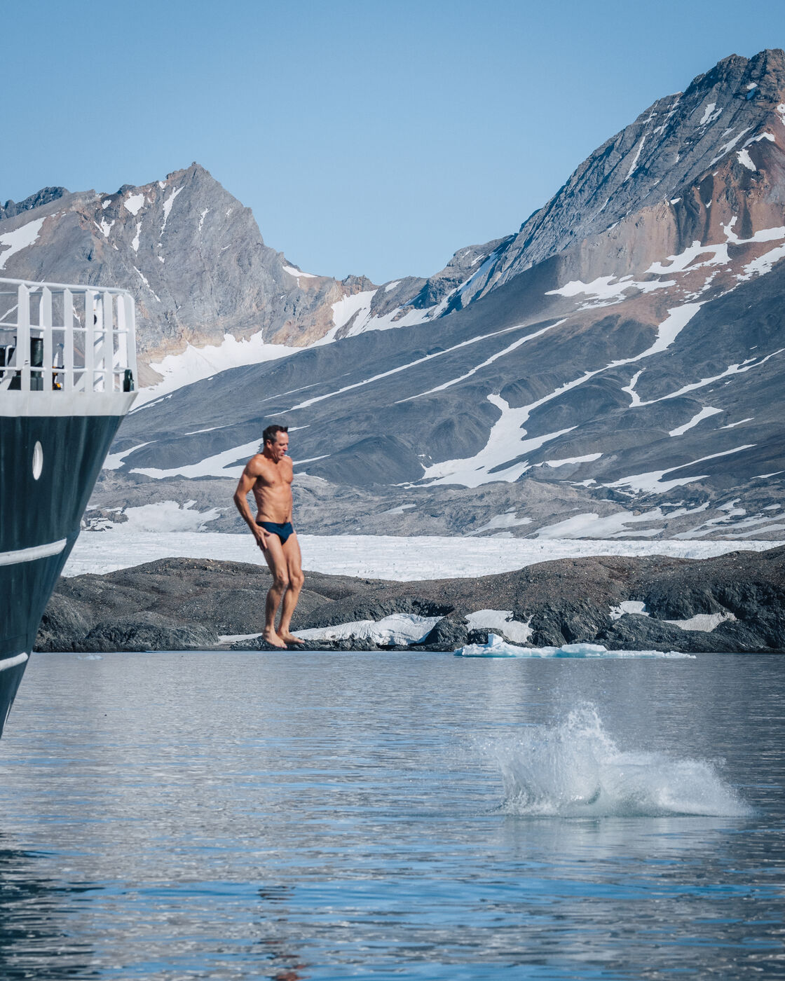 Man in swimming trunks at the ship's side rail, a splash from a jumper below