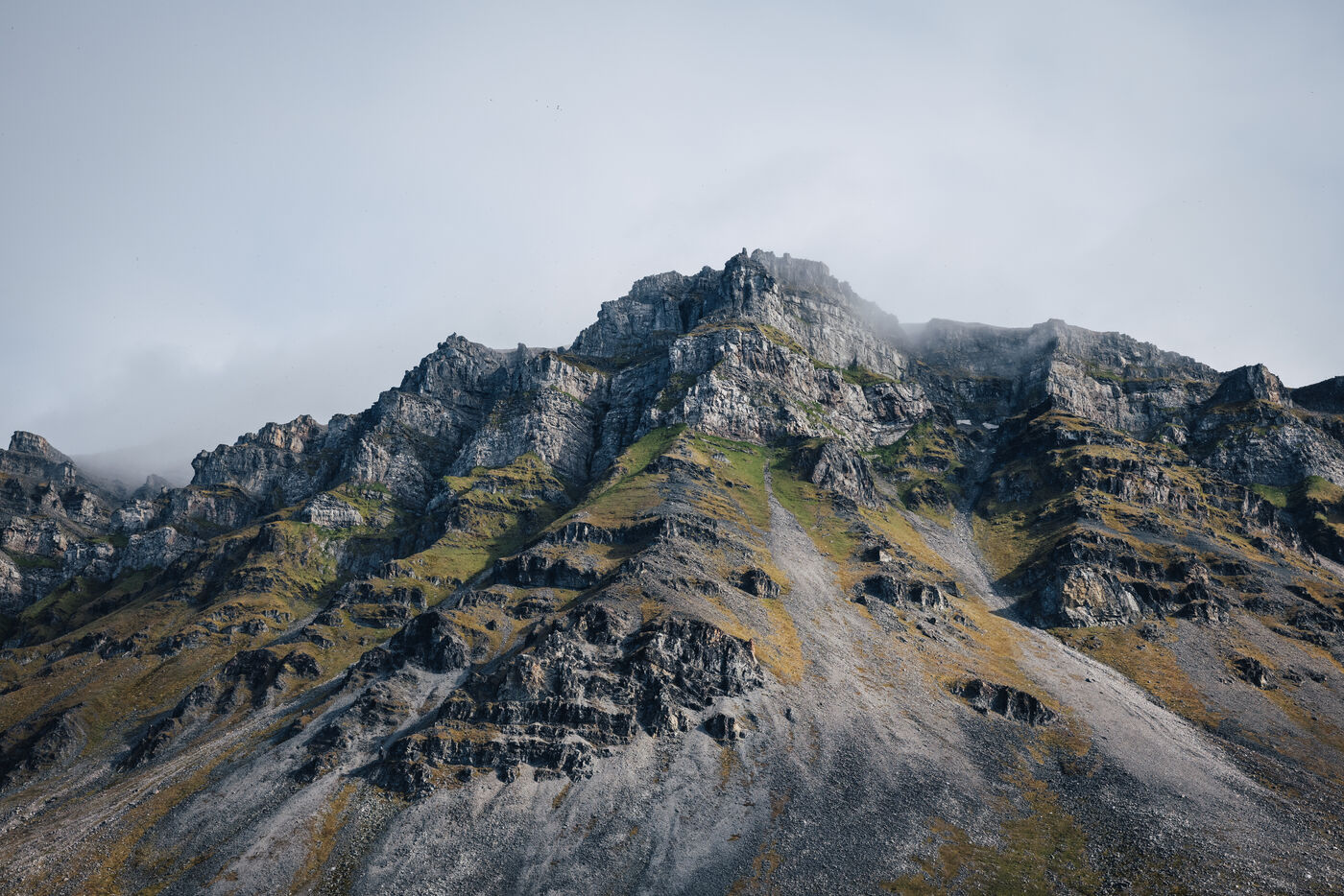 Barren tundra landscape with jagged mountain peak and glacier-carved valleys under cloudy sky