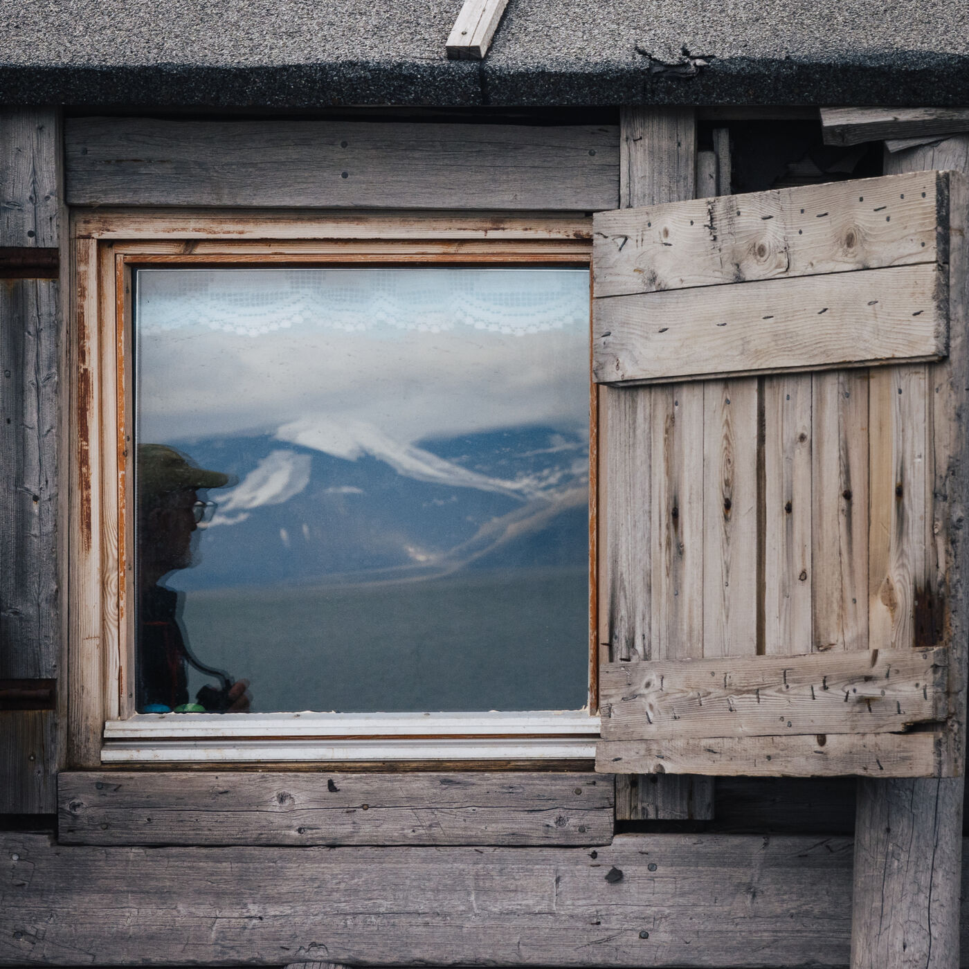 Snow-streaked mountains reflected in the window of a weathered cabin