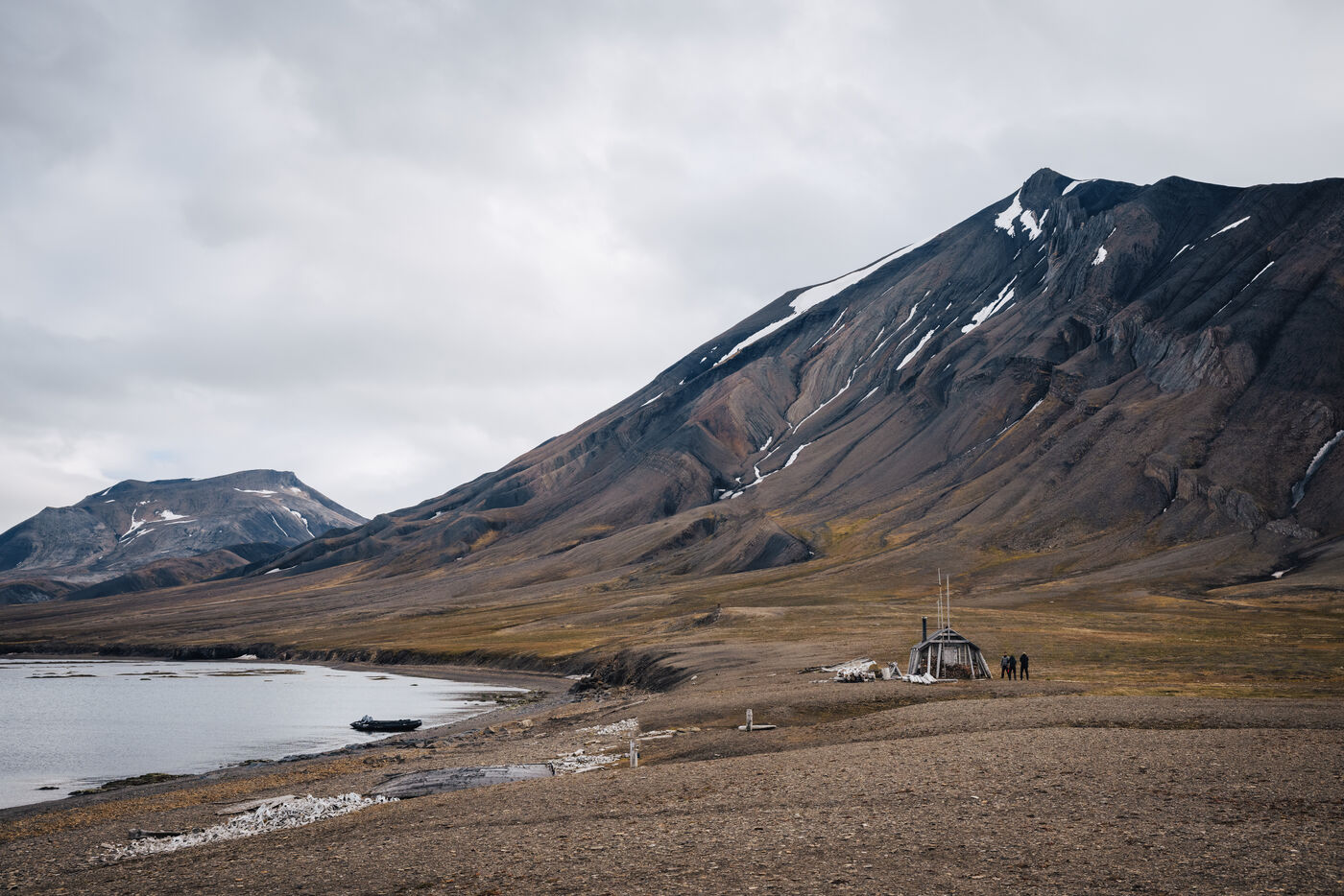 Wide view across the bay to a hut and a small group of people below brown mountains