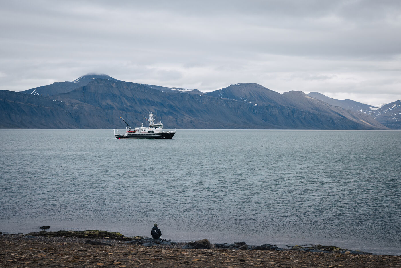 Person standing alone on tundra looking back toward anchored ship in fjord