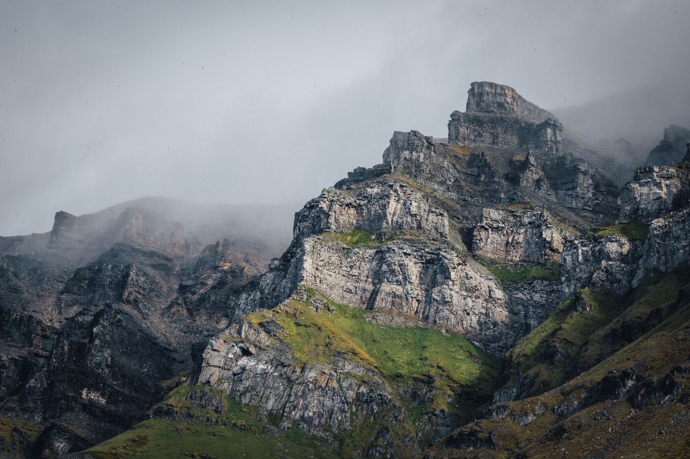 Jagged Arctic mountain peak shrouded in fog above mossy slopes