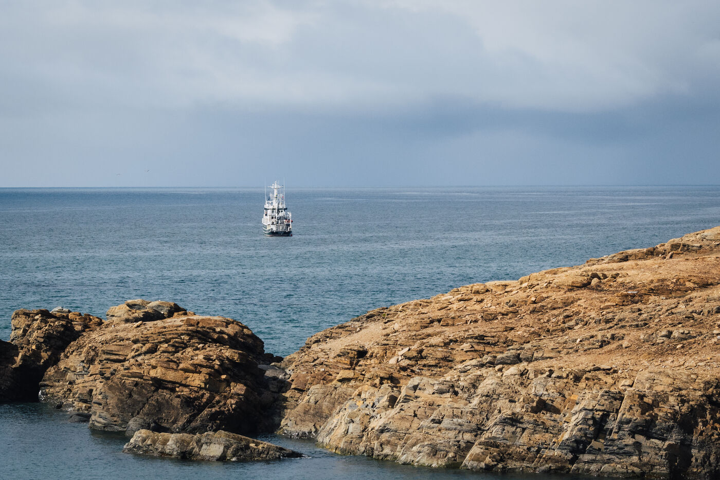 The Kinfish anchored offshore beyond a rocky headland