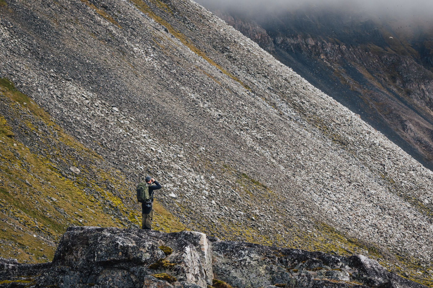 Hiker standing on a rock outcrop below a massive scree slope