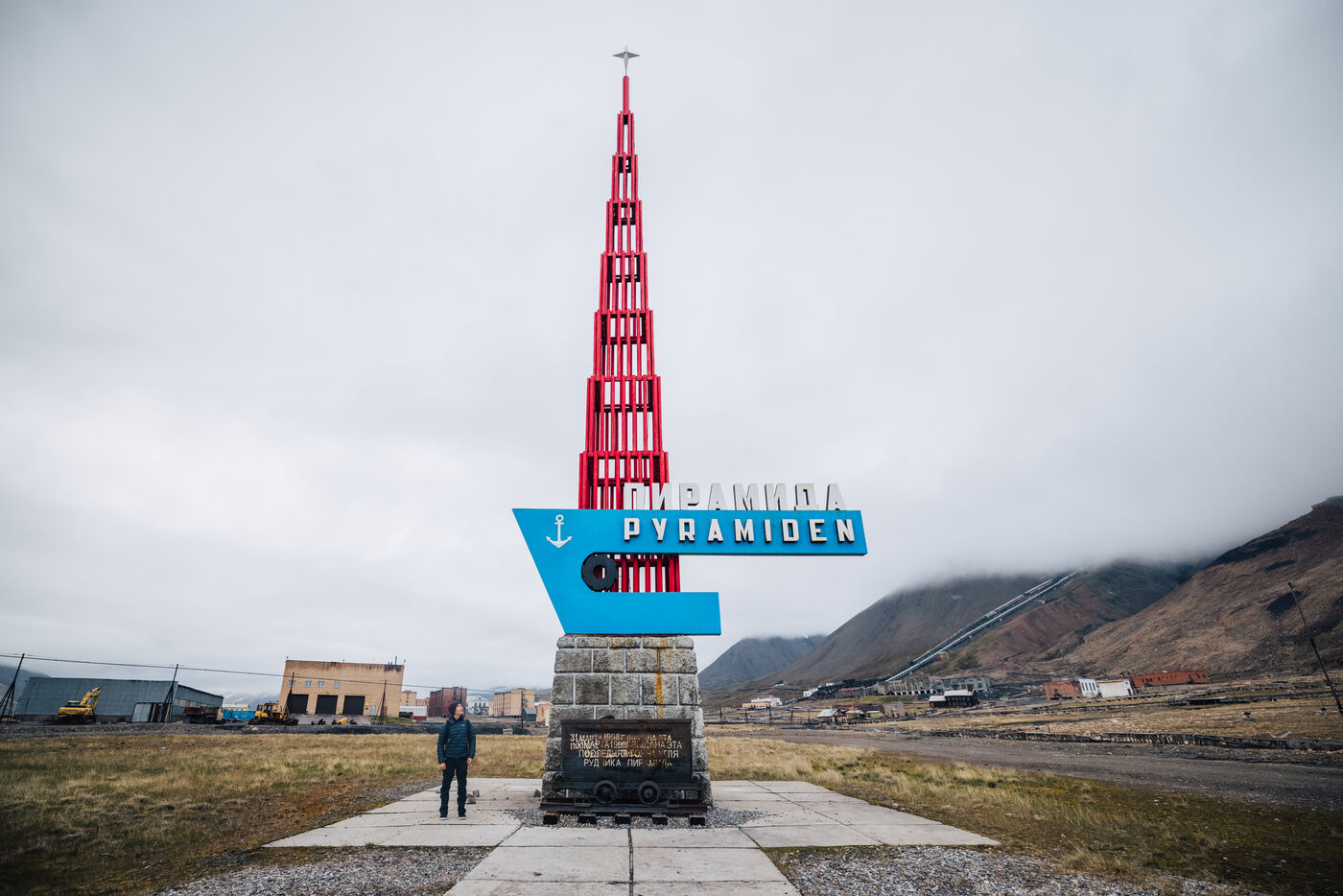 Person standing beneath the Pyramiden sign and its red tower monument