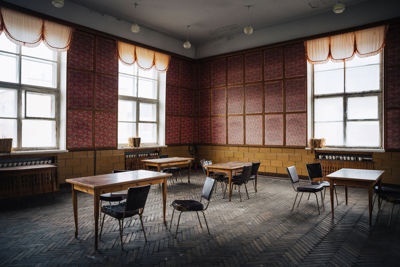 Abandoned canteen with red patterned walls, wooden tables and chairs