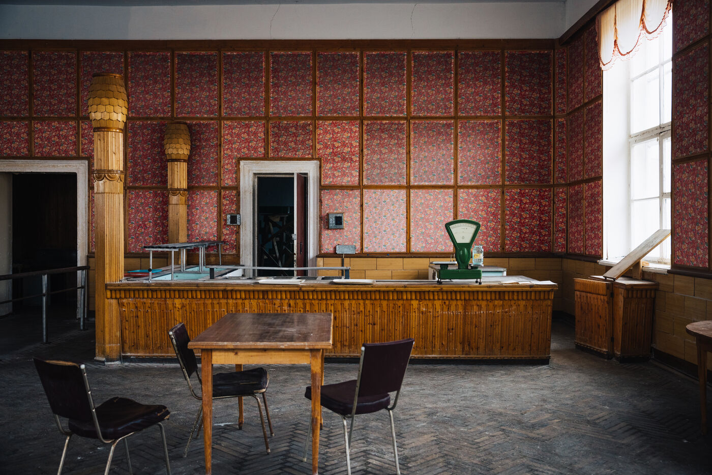 Canteen serving counter with a scale, table and chairs in a red-wallpapered room