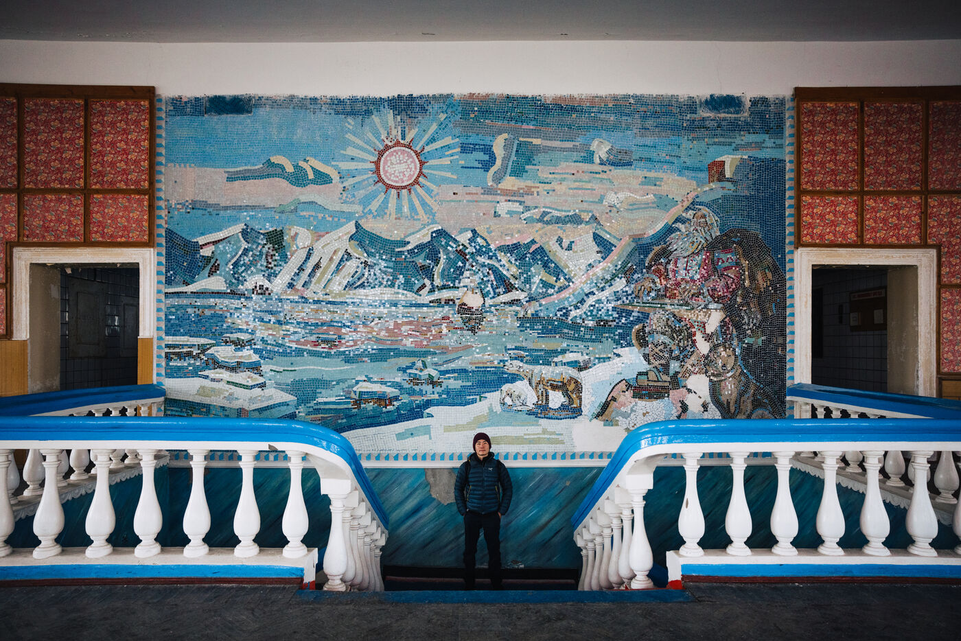 Person standing beneath a Soviet-era mosaic mural of the Arctic, framed by white balustrades