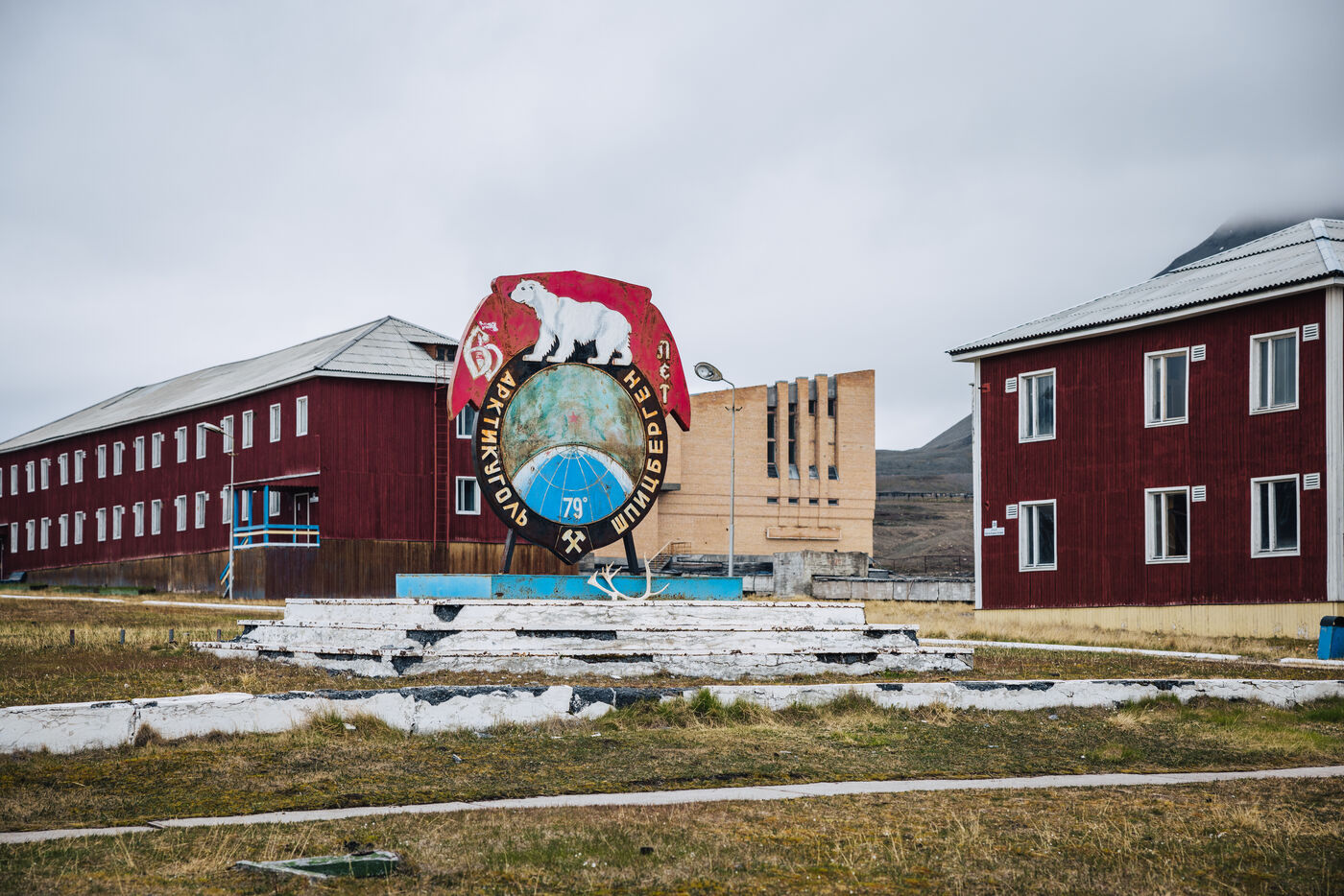Polar bear emblem monument on a plinth between red wooden buildings
