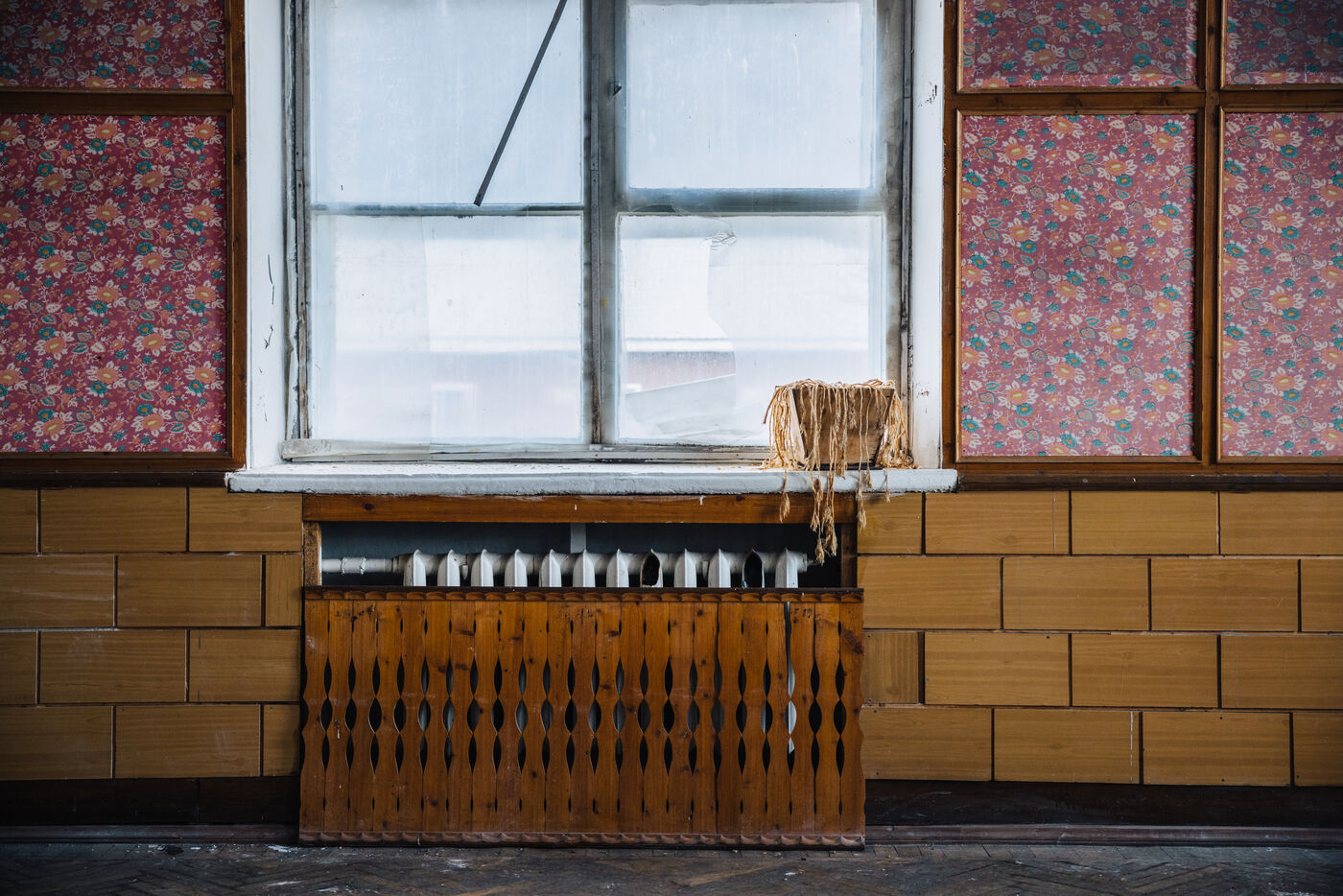 Window with a radiator and a dried plant on the sill in a red-wallpapered room
