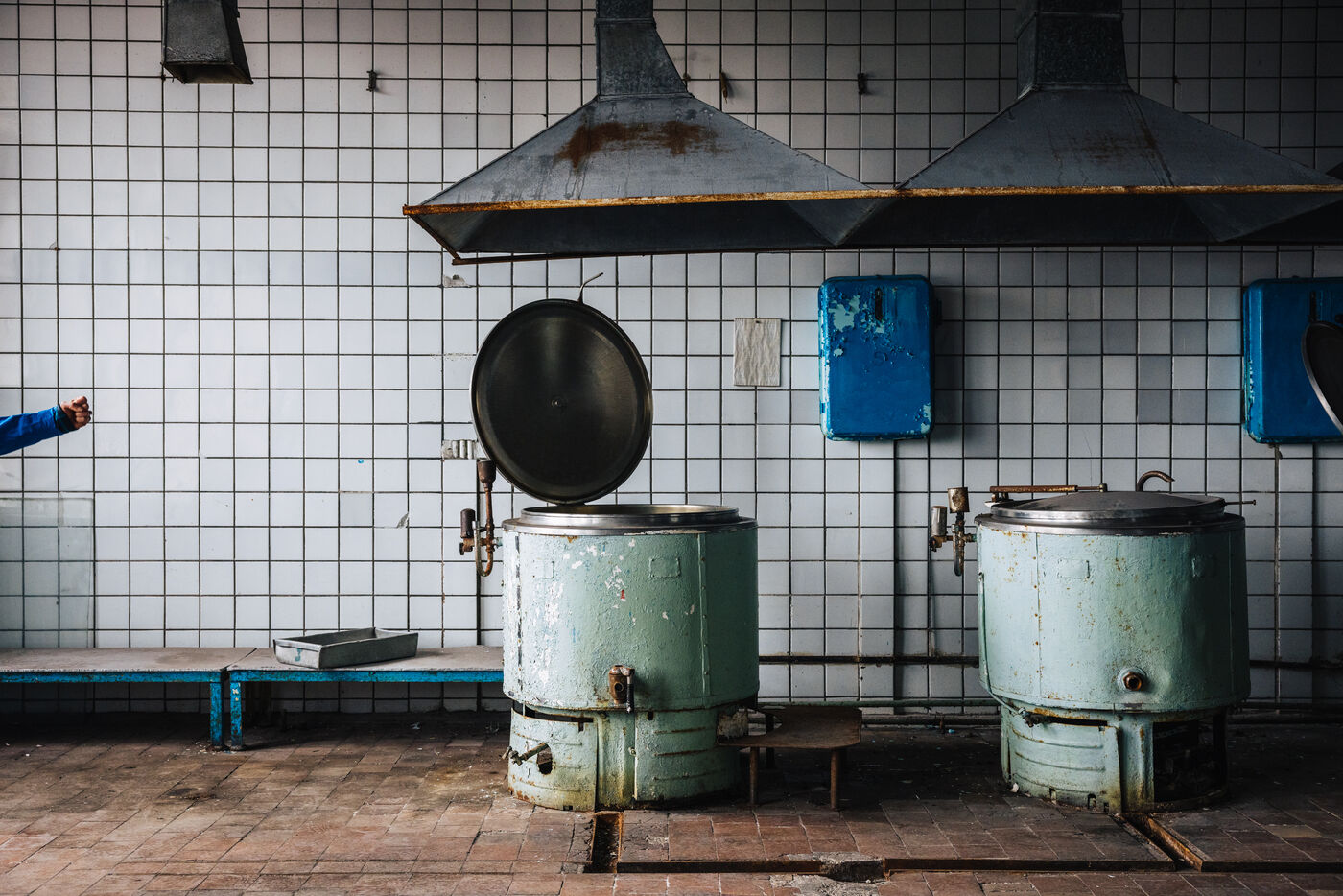 Abandoned kitchen with two green cooking kettles under extractor hoods