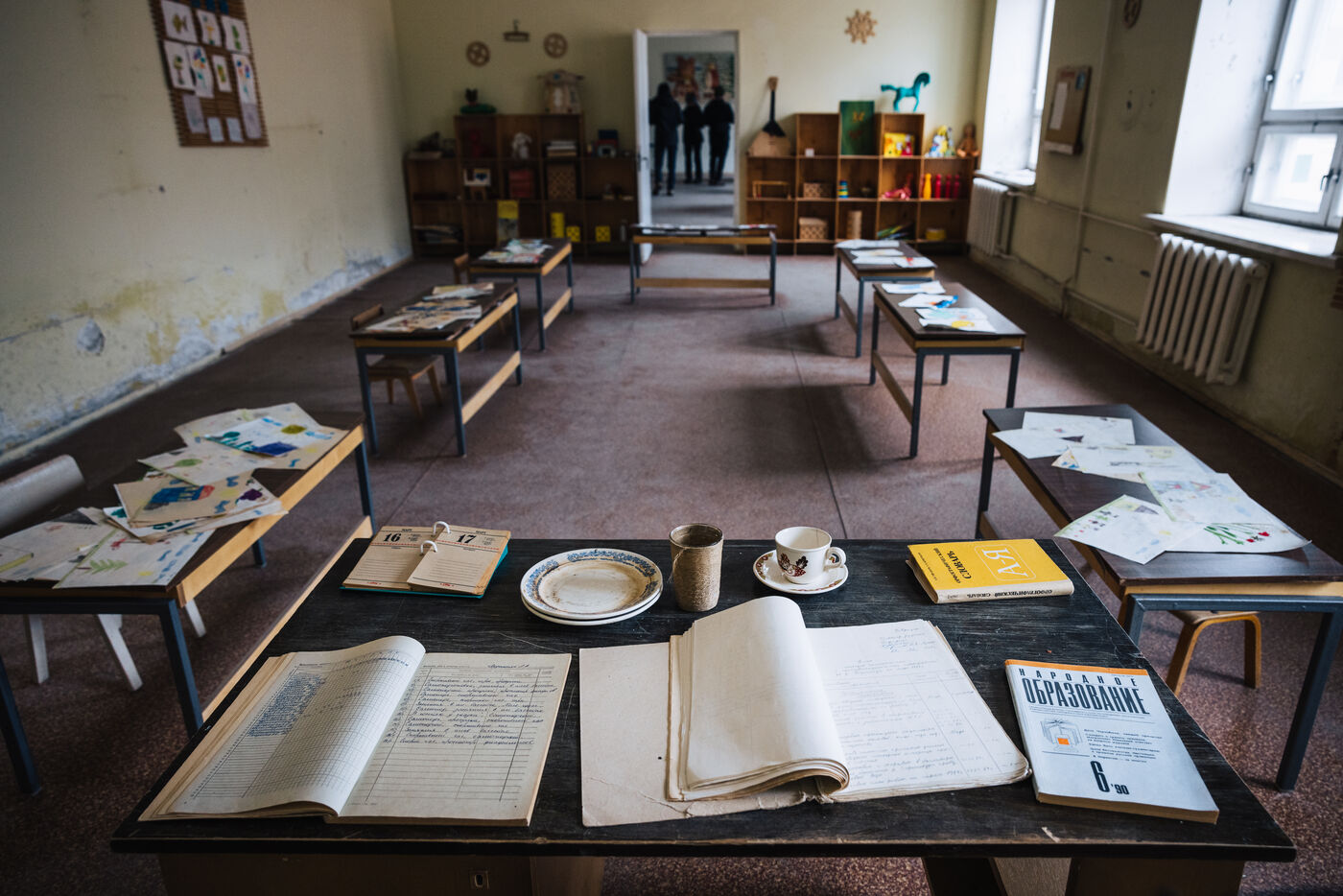 Abandoned classroom with papers and open ledgers scattered across the desks