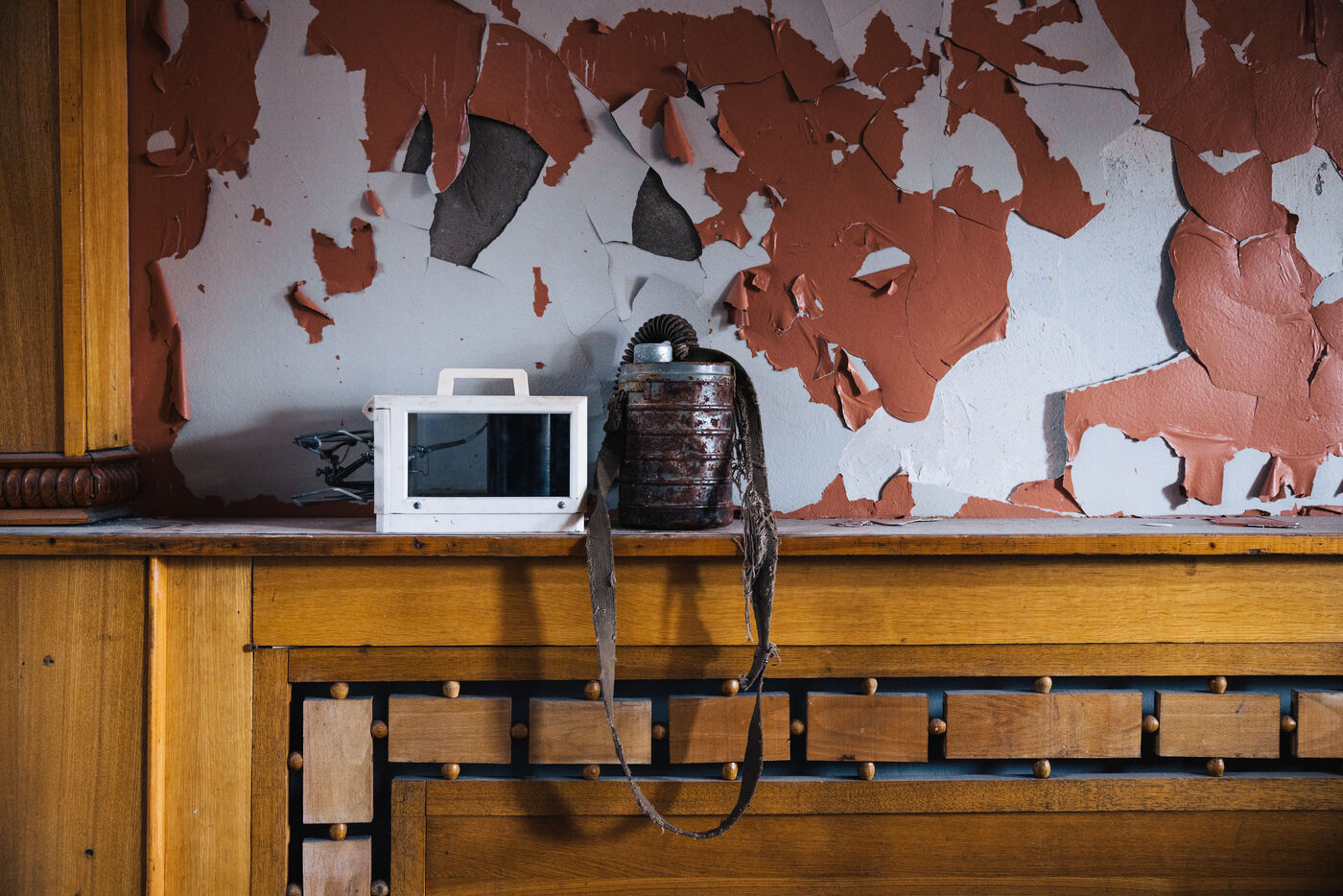 Peeling orange paint above a wooden shelf holding a small television and an old kettle
