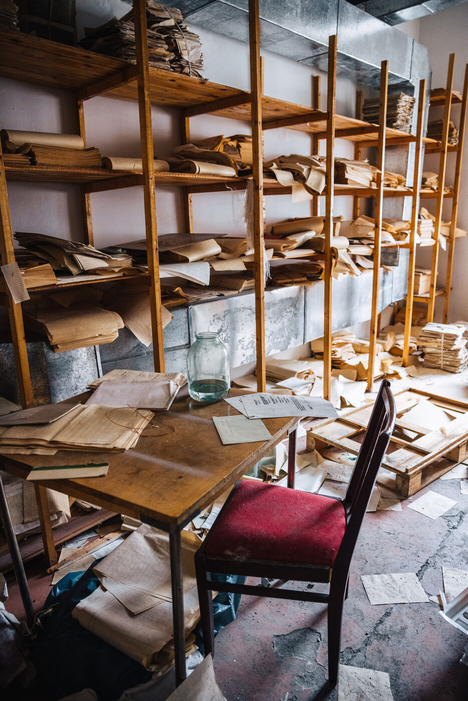 Archive shelves stacked with paper files beside a red chair