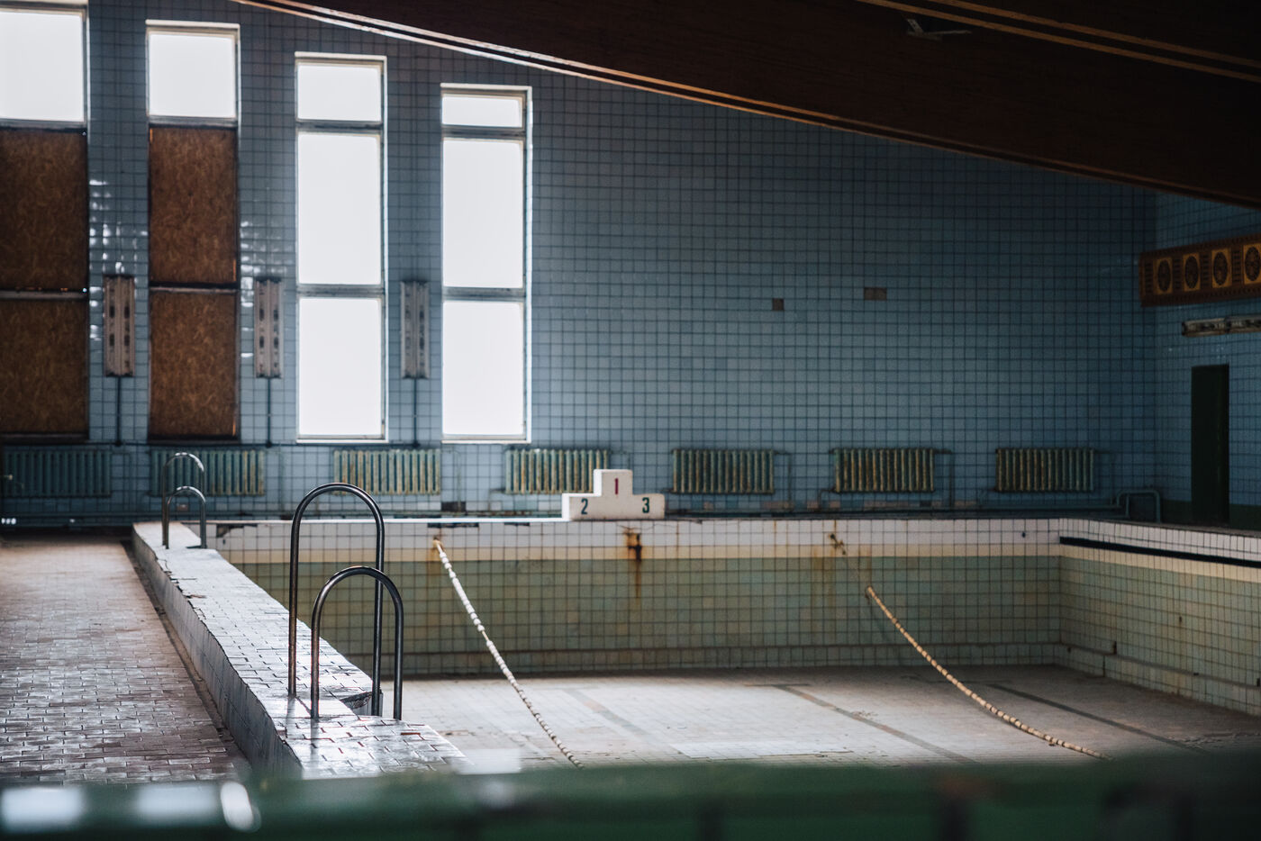 Empty swimming pool with lane ropes still strung beneath tall windows
