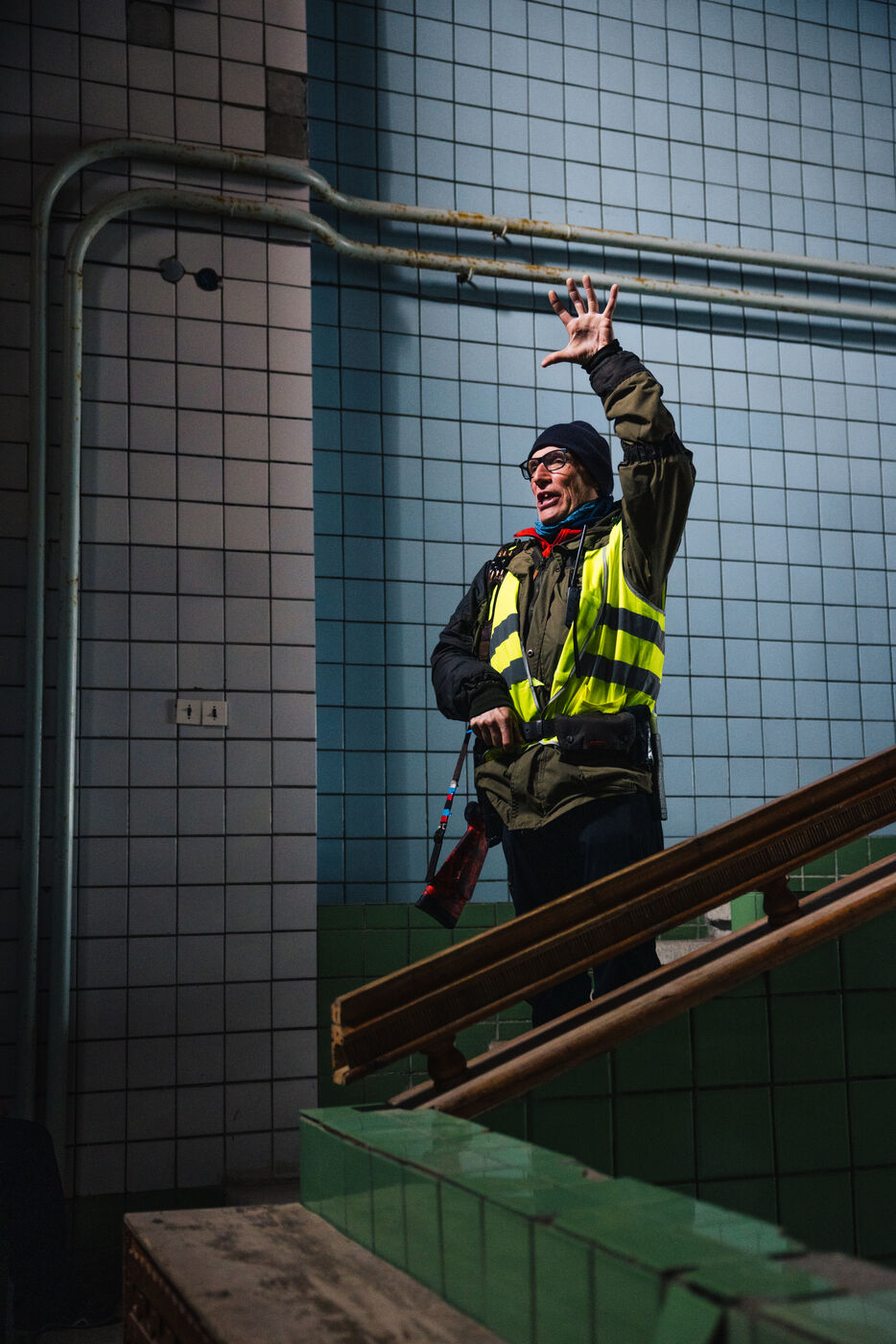 Guide in a reflective vest gesturing on a tiled stairwell