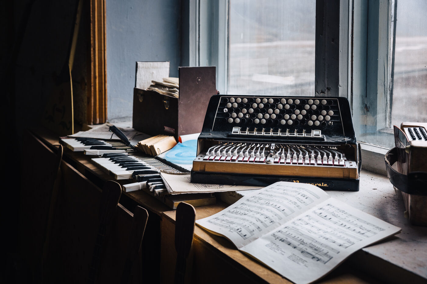 Button accordion resting on a keyboard with sheet music on a windowsill