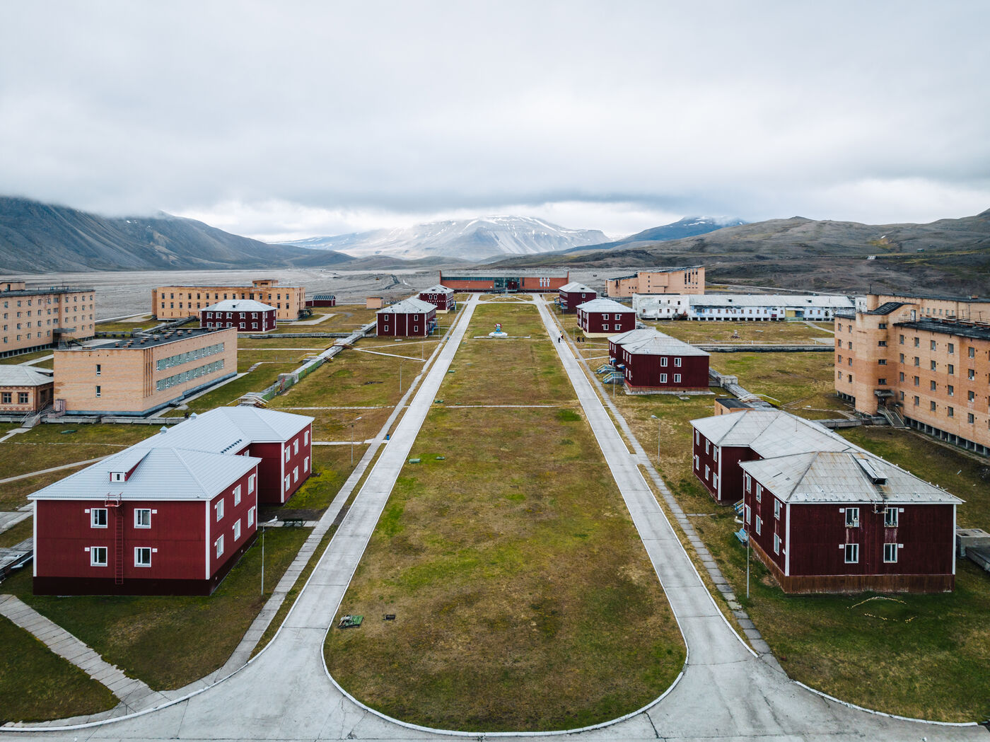 Elevated view down Pyramiden's central green, red buildings on either side and mountains beyond