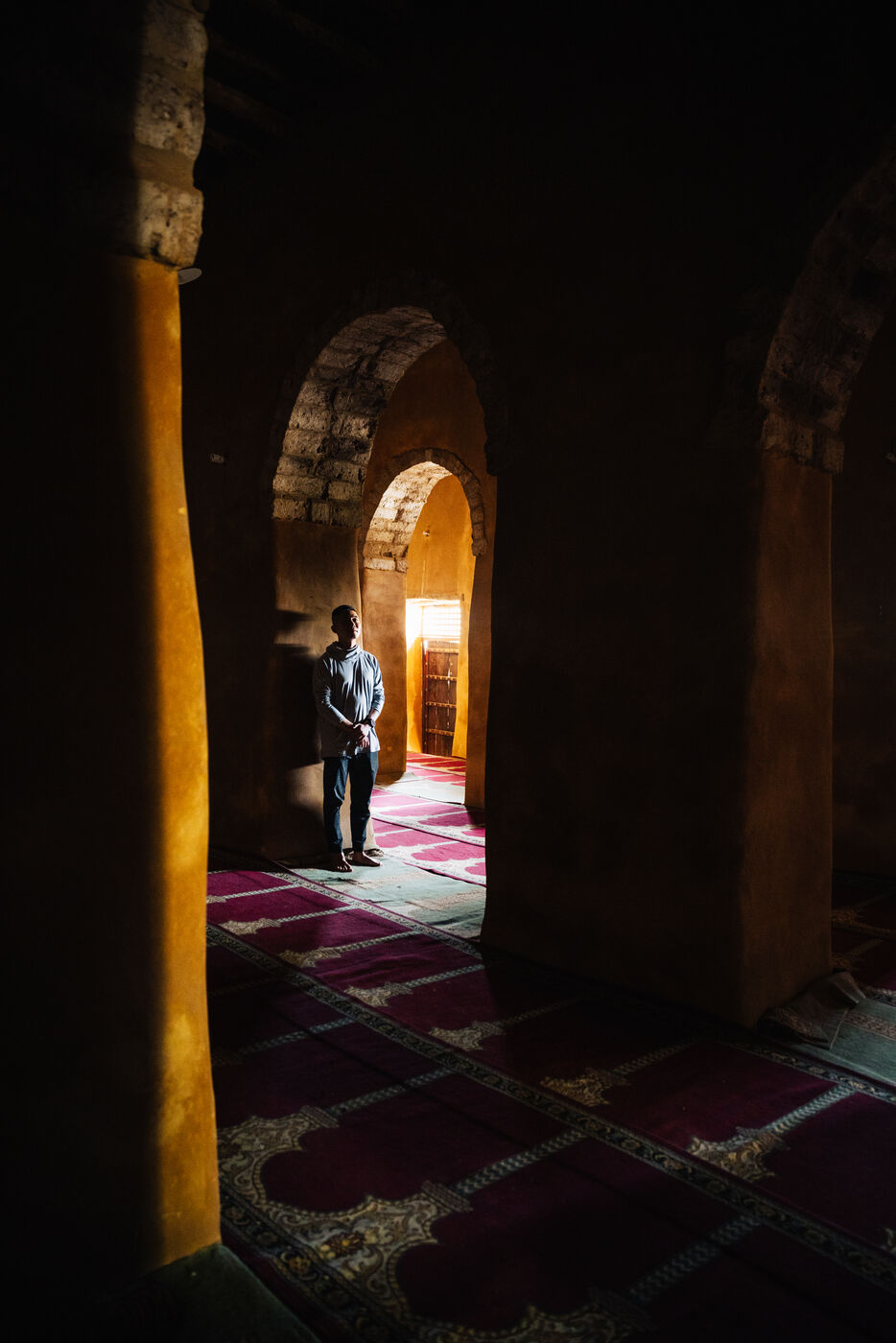 Interior of mosque with light filtering through arched corridors onto prayer rugs