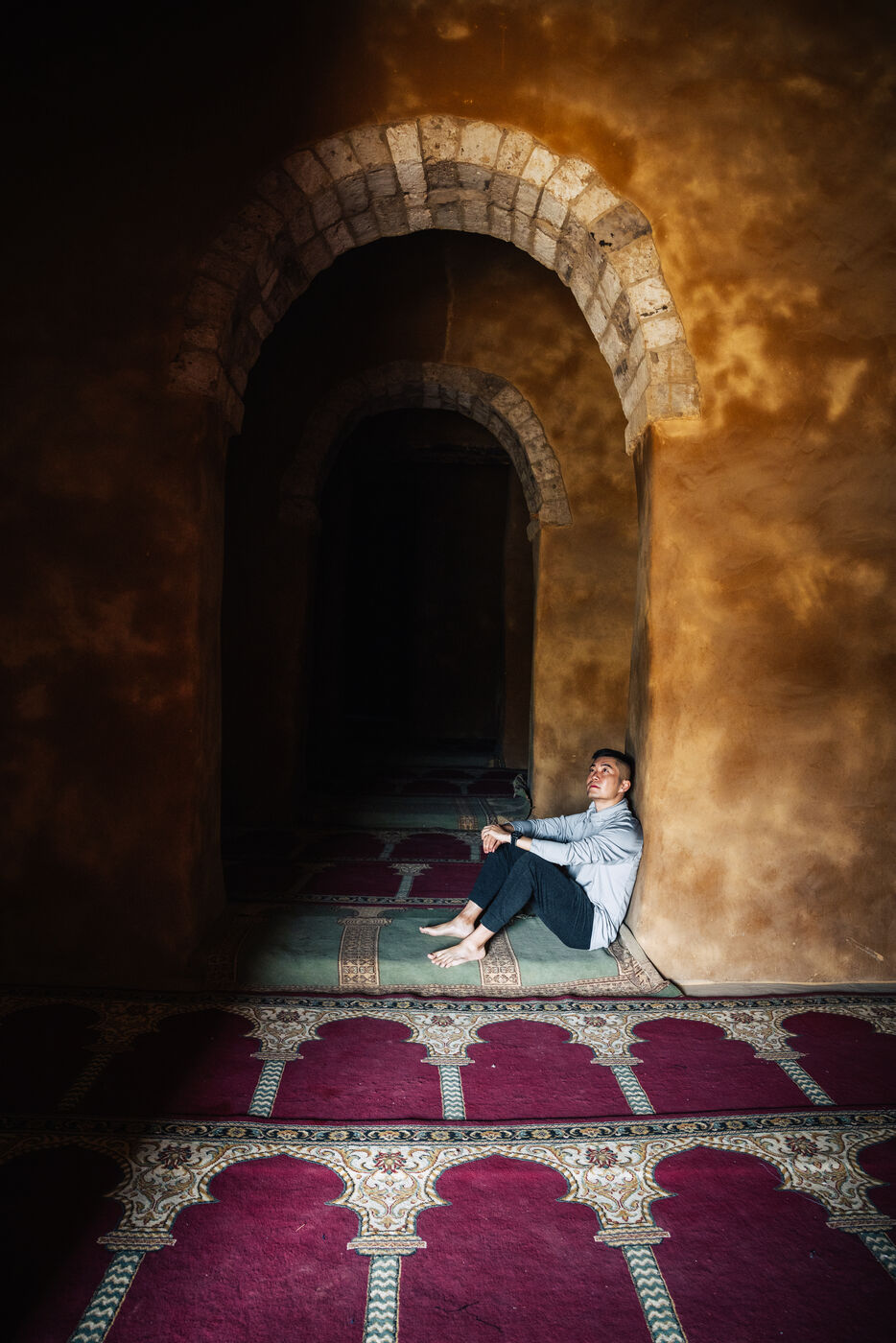 Person sitting inside mosque on prayer rugs